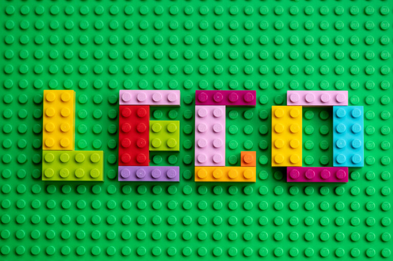 Colorful mosaic letters with Lego text made from Lego bricks on a green base plate background