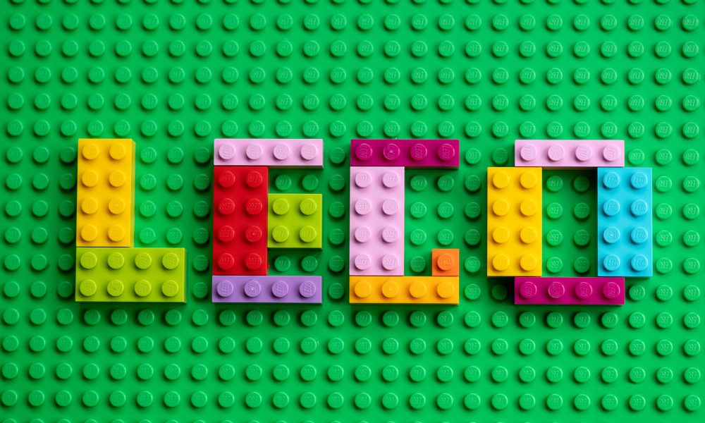 Colorful mosaic letters with Lego text made from Lego bricks on a green base plate background.